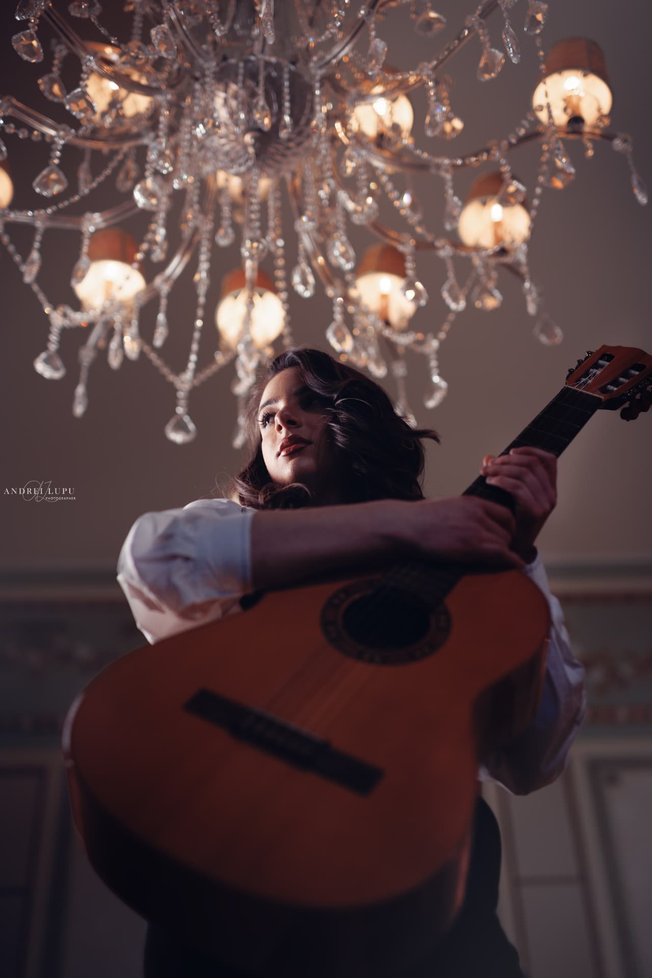 Alexandra Păceană holding her guitar beneath a crystal chandelier